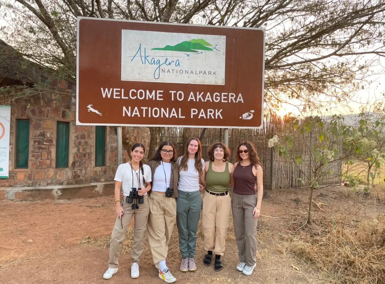 Five guests in safari clothing at the Welcome to Akagera National Park gate sign, Rwanda